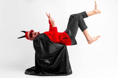 Siyah cadılar bayramı kostümü giymiş tuhaf komik adam ve kafasında şeytan boynuzları asılı beyaz stüdyo arka planında sihirbaz gibi. 