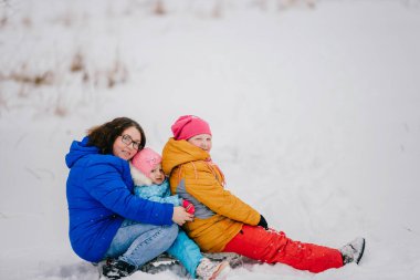 İki komik kızıyla kızağa binen mutlu genç anne. Kışın karlı bir günde dışarıda. Kış eğlencesi.