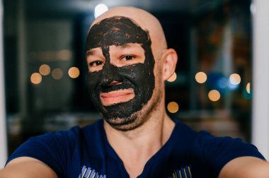 Yüzünde kömür maskesi olan bir adam karanlık arka planda ışıklarla selfie çekiyor..