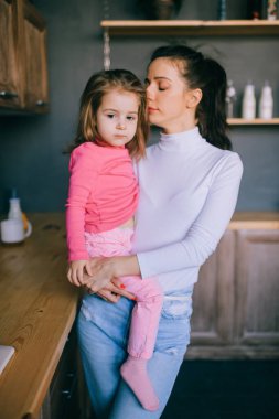 Sevimli genç bayan mutfakta komik kızıyla oynuyor. Güzel bir annenin portresi kucağında taşıdığı ve küçük dişi çocuğunu izlediği. Mutlu aile içinde yaşam tarzı portresi.