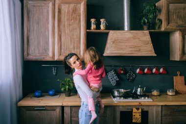 Sevimli genç bayan mutfakta komik kızıyla oynuyor. Güzel bir annenin portresi kucağında taşıdığı ve küçük dişi çocuğunu izlediği. Mutlu aile içinde yaşam tarzı portresi.