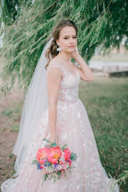 Beyaz gelinlik içinde güzel bir gelin elinde çiçeklerle dışarıda poz veriyor..