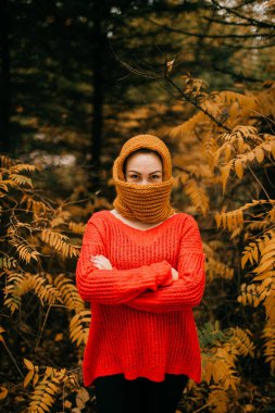 Kırmızı ceketli, siyah pantolonlu çekici bir kadın soğuk sonbahar ormanlarında ısınmak için kafasına atkı takmış..