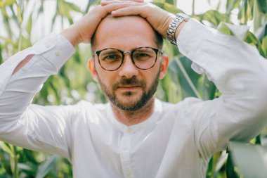 Kısa sarı saçlı, yüzünde gözlüklü siyah tüyler ve mısır tarlasında yürüyen beyaz gömlekli çekici, yalnız beyaz bir adam.