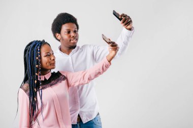 Mutlu Afro-Amerikan çifti beyaz arka planda akıllı telefonlu selfie çekiyor.