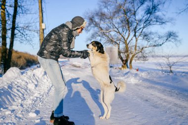 Yetişkin ve mutlu bir adam kar yolunda dost canlısı bir köpekle poz veriyor.