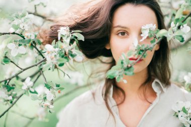 Çiçek açan bahar elma ağaçları. Şefkat, kolaylık ve kadınlık. Genç güzel esmer kız güzel doğada çiçeklerin tadını çıkarıyor. Şirin, mutlu, genç bir bayan bahçede dinleniyor.