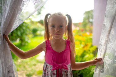 Beyaz saçlı, uzun boylu, pembe elbiseli bir kız köyün evine girer ve gülümser.