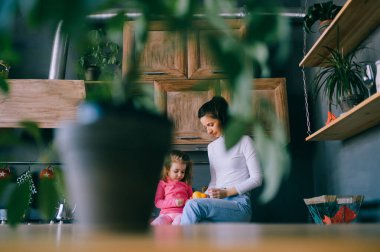 Sevimli genç bayan mutfakta komik kızıyla oynuyor. Güzel bir annenin portresi kucağında taşıdığı ve küçük dişi çocuğunu izlediği. Mutlu aile içinde yaşam tarzı portresi.