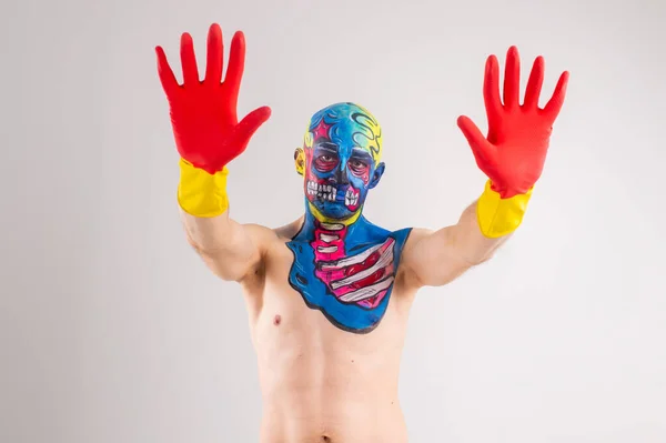 Portrait of a strange man with makeup on his head and shoulder in red-yellow gloves, black pants and boots, no T-shirt