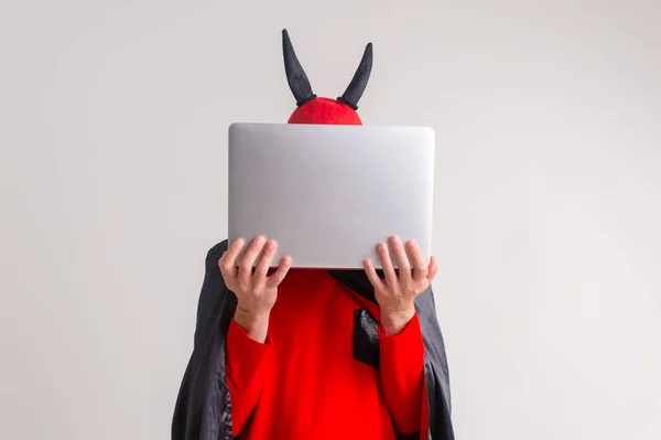 スタイリッシュなCaucasian男で悪魔の帽子とともに角と吸血鬼ケープとともにラップトップ隔離された白い背景 — ストック写真