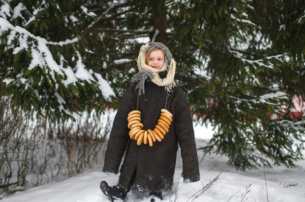可愛い白人の村の女の子は冬に乾燥したリング状のロールサンドの笑顔で雪の森の中に立っています — ストック写真