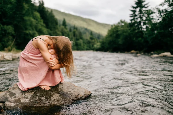 忧心忡忡的小女孩坐在河边的石头旁 — 图库照片