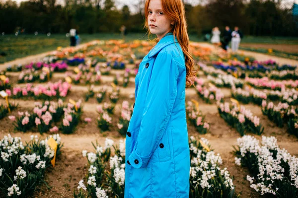 青いコートに赤い髪のかわいい女性の子供は大きな庭に立っています — ストック写真