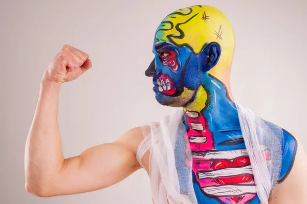 A strange man with makeup on his head and shoulder in white t-shirt shows his muscles and biceps