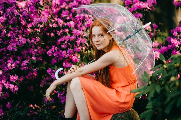 奇怪的小女孩 红头发 漂亮的脸蛋 穿着夏天橙色的衣服 在花园里拿着一把雨伞 — 图库照片