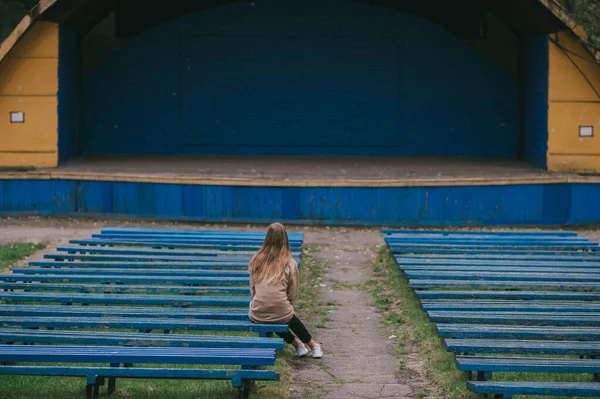 一个孤零零的女孩坐在露天剧场的长椅上 背对着一排排的针尖长椅和场景 — 图库照片