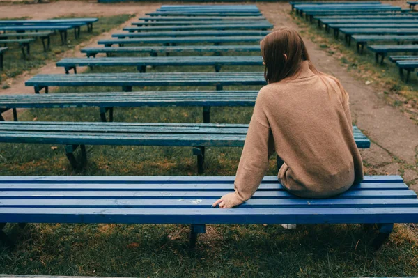 一个孤独的女孩坐在长椅上 背靠着一排荒凉的长椅的背像 — 图库照片