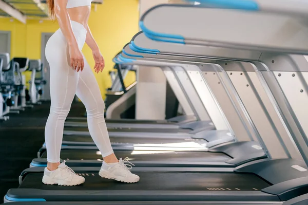 young sport woman running on treadmill in gym, keeps fit, burn calories on running machine, wearing white sportswear and sneakers