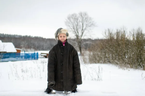 Emotional portrait of positive slavonic girl wearing loose fit padded jacket with scarf on her head in winter snowy day in village