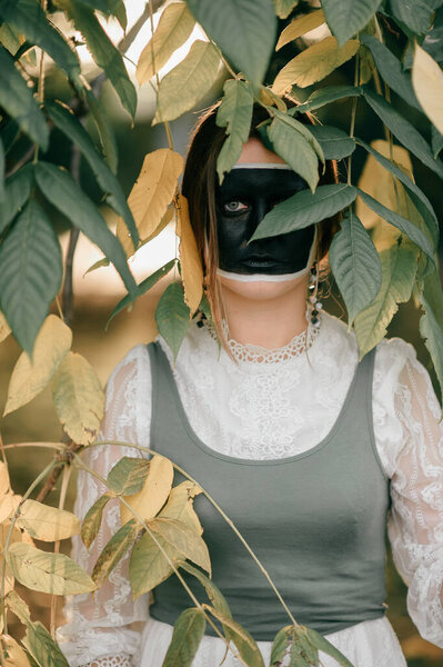 Portrait of  adult woman in old fashioned  white dress and black square painted on her face. Creative face art.