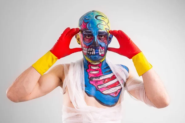 Strange man with makeup on his head and shoulder in white t-shirt, red and yellow gloves, red trousers thinks about something and hypnotizes you