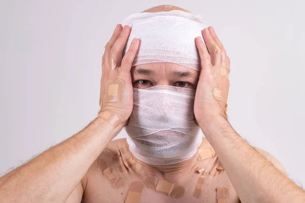 Injured man with many patches on his body and bandaged head isolated on white background
