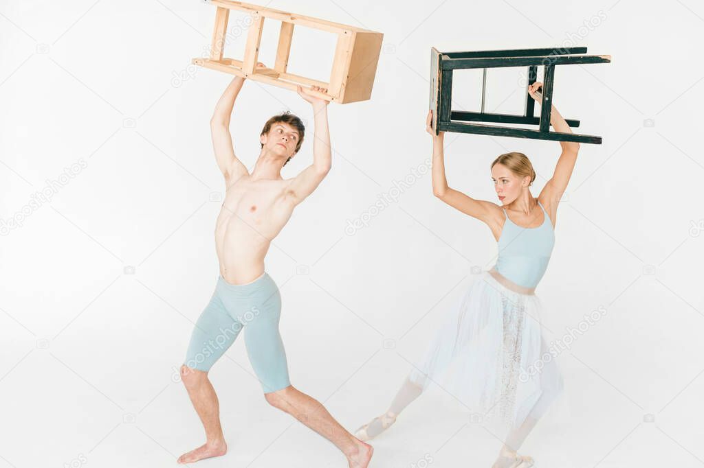 Funny and unusual couple of modern ballet dancers posing with chair in hands above their heads