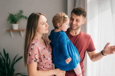 Güzel anne ve yakışıklı baba güzel küçük kızıyla parlak bir odada eğleniyor ve gülümsüyor.