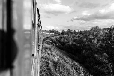 Yazın trenle gezmekten pencere dışındaki manzara. Tepeler, dağlar ve ormanlar. Tatil ve seyahat konsepti. Tren vagonlu lokomotif tren yolu boyunca ilerliyor.