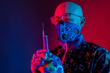 Solunum maskesi ve gözlük takan şık kel bir adam elinde kırmızı mavi arka planda, kovid 19 'a karşı aşıyla bir şırınga tutuyor. Coronavirus konsepti