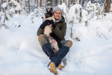 Karlı ormanda sevimli köpeği elinde tutan mutlu bir adam. Kış ormanında sevimli köpek yavrusuna sarılan gülümseyen çocuk. Hayvan sever. Köpek - insanın arkadaş konsepti.