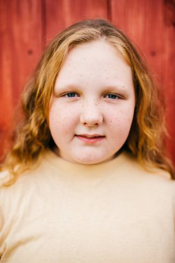 Sarı tişörtlü uzun saçlı neşeli tombul kızın portresi ahşap arka planda izole edilmiş bir köyde duruyor.