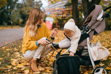 Büyük mavi gözlü, kısa kızıl saçlı, güzel mutlu annesiyle sonbaharda bebek arabasında dudaklarını pompalayan güzel bir bebek.
