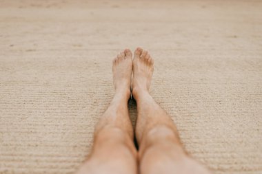 Kumsalda erkek ayakları. Deniz kıyısındaki beyaz kumda dinlen. Yetişkin bir erkeğin iki bacağı okyanusun kenarında gevşek kumda yatıyor.