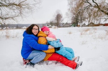 İki komik kızıyla kızağa binen mutlu genç anne. Kışın karlı bir günde dışarıda. Kış eğlencesi.