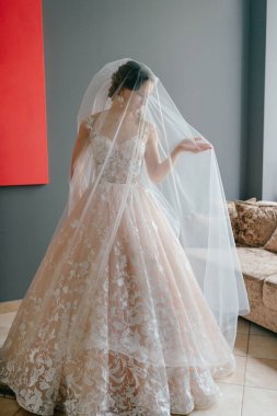 Gri arka planda, elinde çiçekle poz veren beyaz elbiseli güzel gelinin portresi.