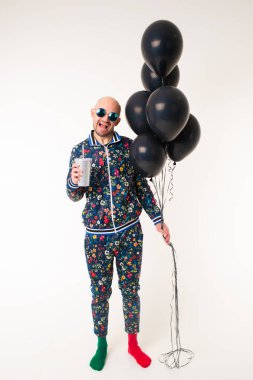 Çok renkli eşofmanlı, kırmızı ve yeşil çoraplı beyaz bir adam siyah toplar tutuyor ve parlak bardaklardan bir kokteyl içiyor..