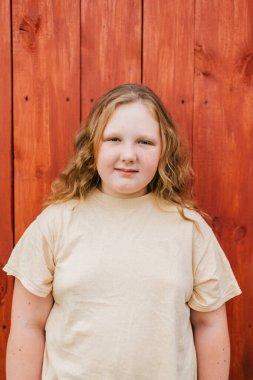 Sarı tişörtlü uzun saçlı neşeli tombul kızın portresi ahşap arka planda izole edilmiş bir köyde duruyor.