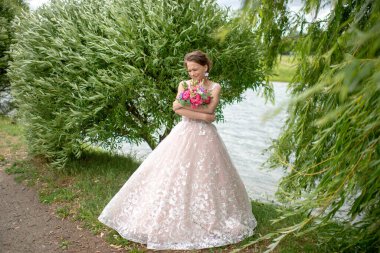 Beyaz gelinlik içinde güzel bir gelin elinde çiçeklerle dışarıda poz veriyor..