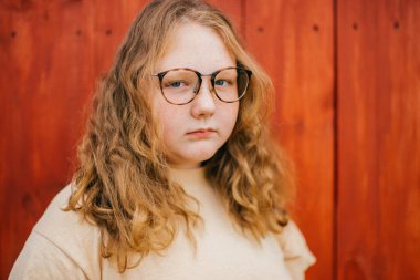 Sarı tişörtlü, uzun saçlı neşeli tombul bir kızın portresi. Gözlükler köyde duruyor. Ahşap arka planda izole edilmiş.