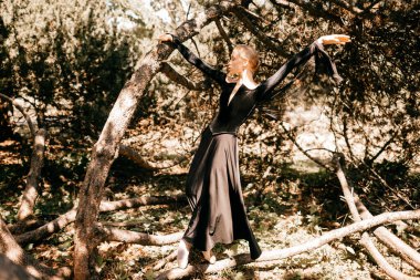 Siyah bir elbise içinde, ağaçların arasında poz vermiş güzel bir balerin..