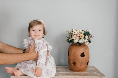 Beyaz tenli yakışıklı, güçlü bir baba, parlak bir odada, rafta oturan küçük tatlı kızını tutuyor.