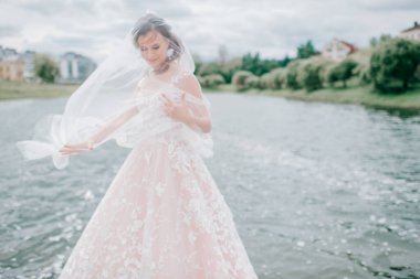 Yüzü peçeyle örtülmüş, arka planda gölle dışarıda poz veren gelinlik giymiş güzel bir gelin..