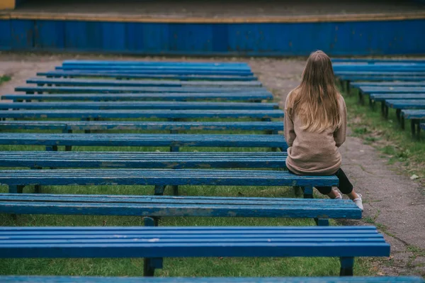 一个孤独的女孩坐在长椅上 背靠着一排荒凉的长椅的背像 — 图库照片