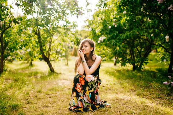 夏のライラックガーデンで長い髪とカラフルなドレスで幸せと魅力的な美しい芸術的な若いモデルの女の子は 茂みやカメラのポーズ花を持つ 春のコンセプト — ストック写真