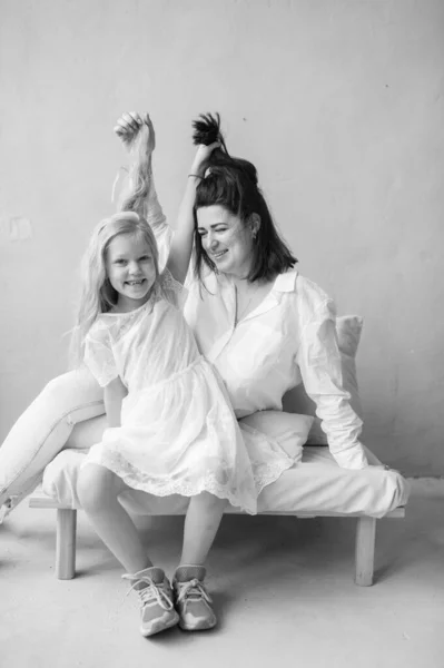 Mother and daughter indoor lifestyle black white portrait. Mom with child have fun in studio. Happiness of motherhood. Mother hugs with her little daughter. Young emotional girl  embraces her mom