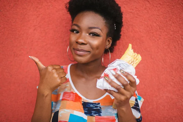 Neşeli Afro Amerikalı Kız Elinde Hamburgerle Arka Plandaki Kırmızı Duvarın — Stok fotoğraf