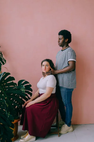 Loving interracial couple lifestyle portrait. Dark skinned african man holding neck of his caucasian girlfriend on pink wall background.  Black man and white woman relationship. Strange friednship