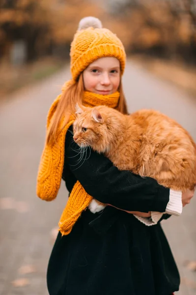 Little caucasian girl with freckles face holding her fat cat in autumn park.